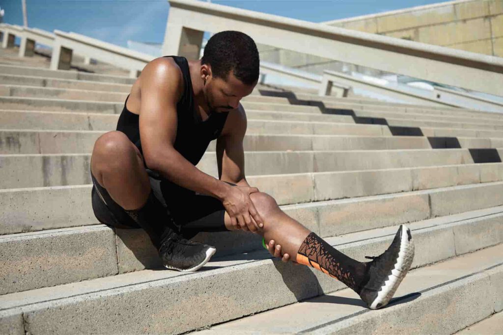 Young man on the stairs, holding his knee with both hands while he's sitting down